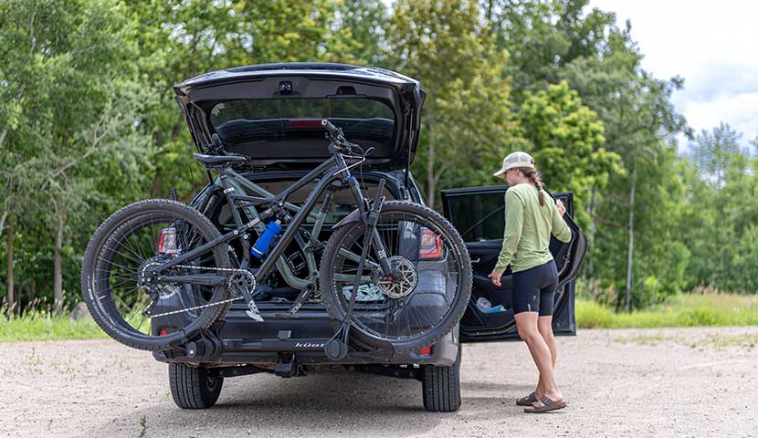 Person loading a bicycle onto a car with a bike rack in a natural setting.