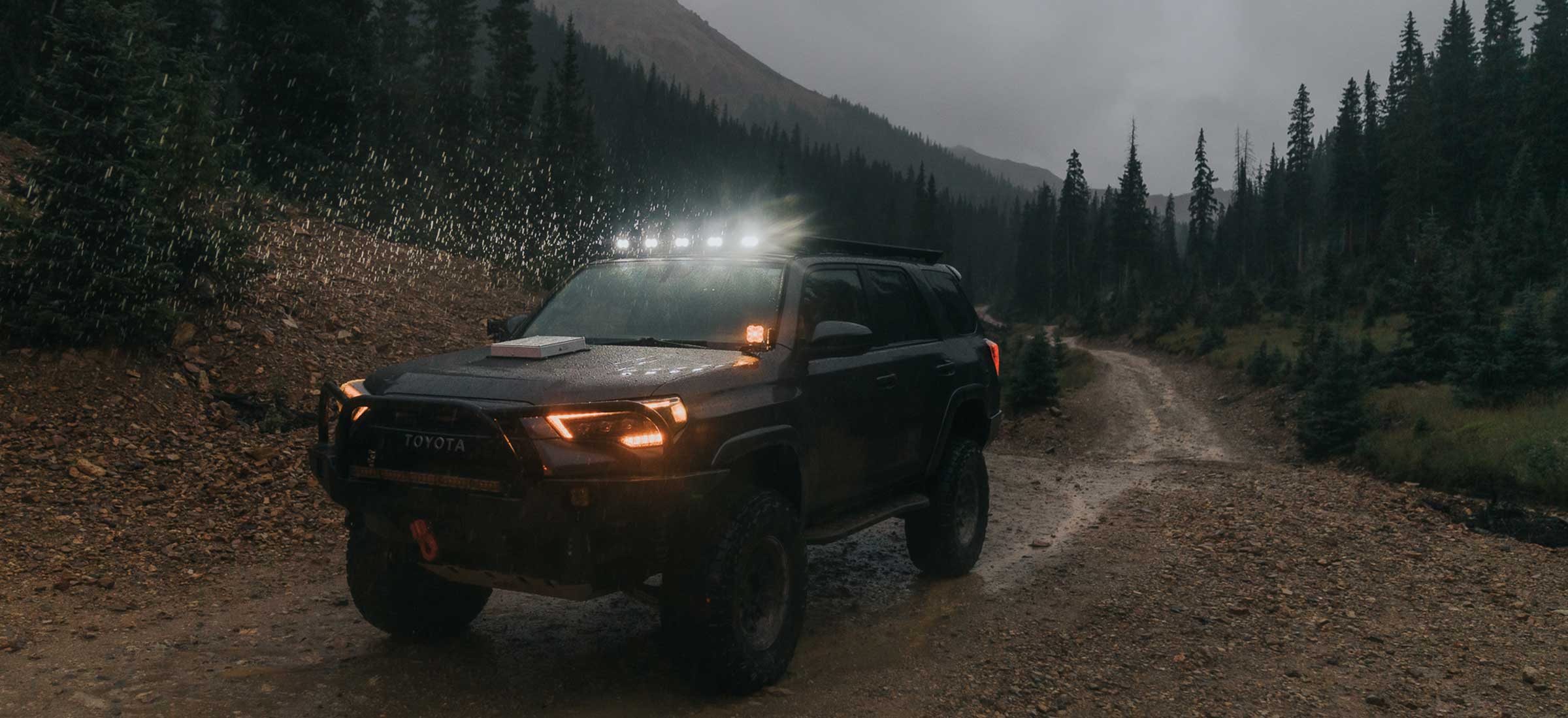 Off-road vehicle on a dirt road in a forested area with mountains in the background